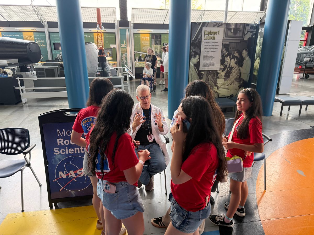 Tripulantes conversando con un científico espacial en la sala del cohete Saturno V