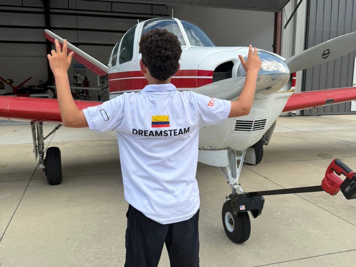 Tripulante de espaldas con la camiseta Dream STEAM y la bandera de Colombia frente a una avioneta
